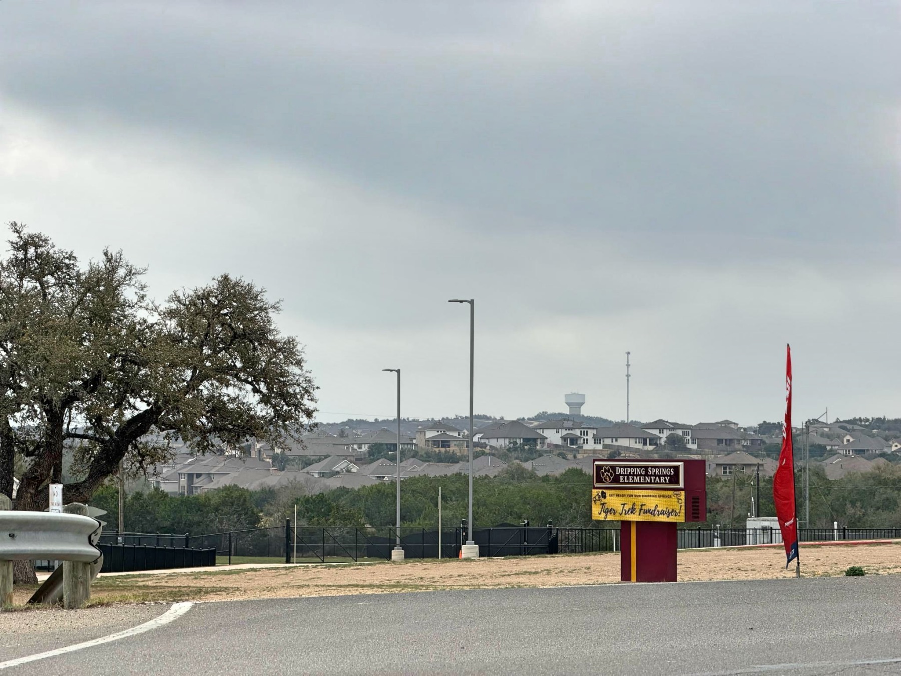 Dripping Springs Elementary School sign with Tiger Trek Fundraiser announcement, surrounded by Texas Hill Country landscape and residential neighborhood in Dripping Springs ISD