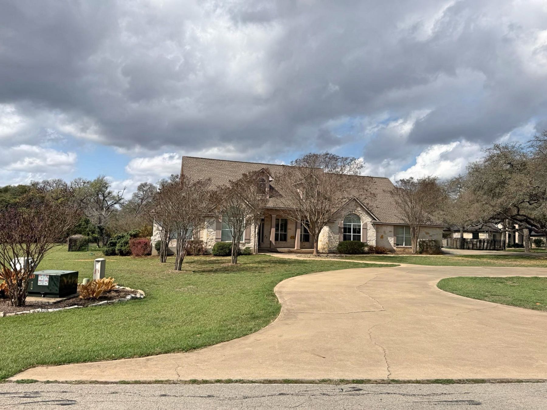 Stone home with circular concrete driveway surrounded by mature trees in Hidden Springs Ranch Dripping Springs TX 78620