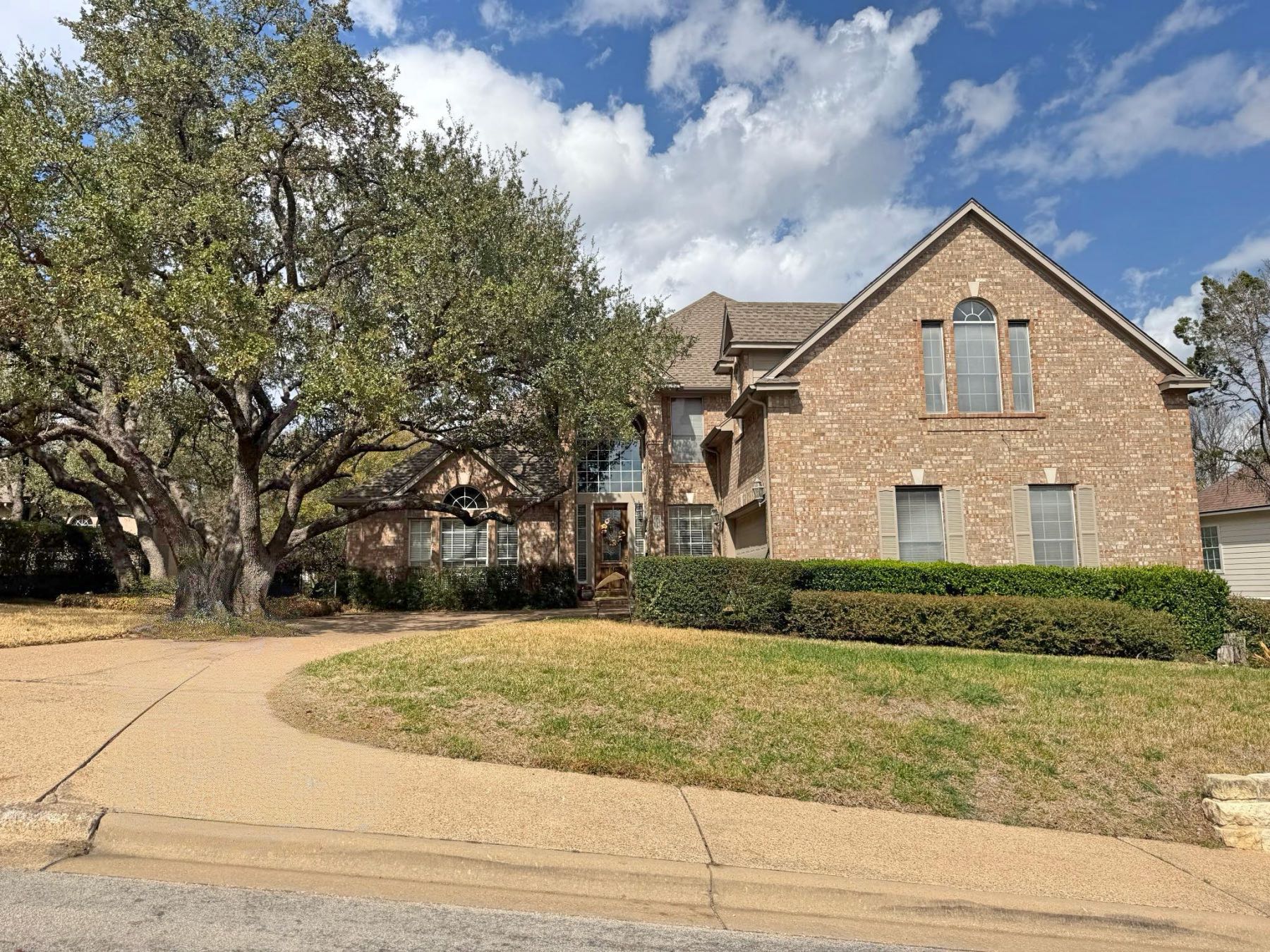Two-story brick home with curved driveway and two-car garage in Senna Hills Austin TX 78733