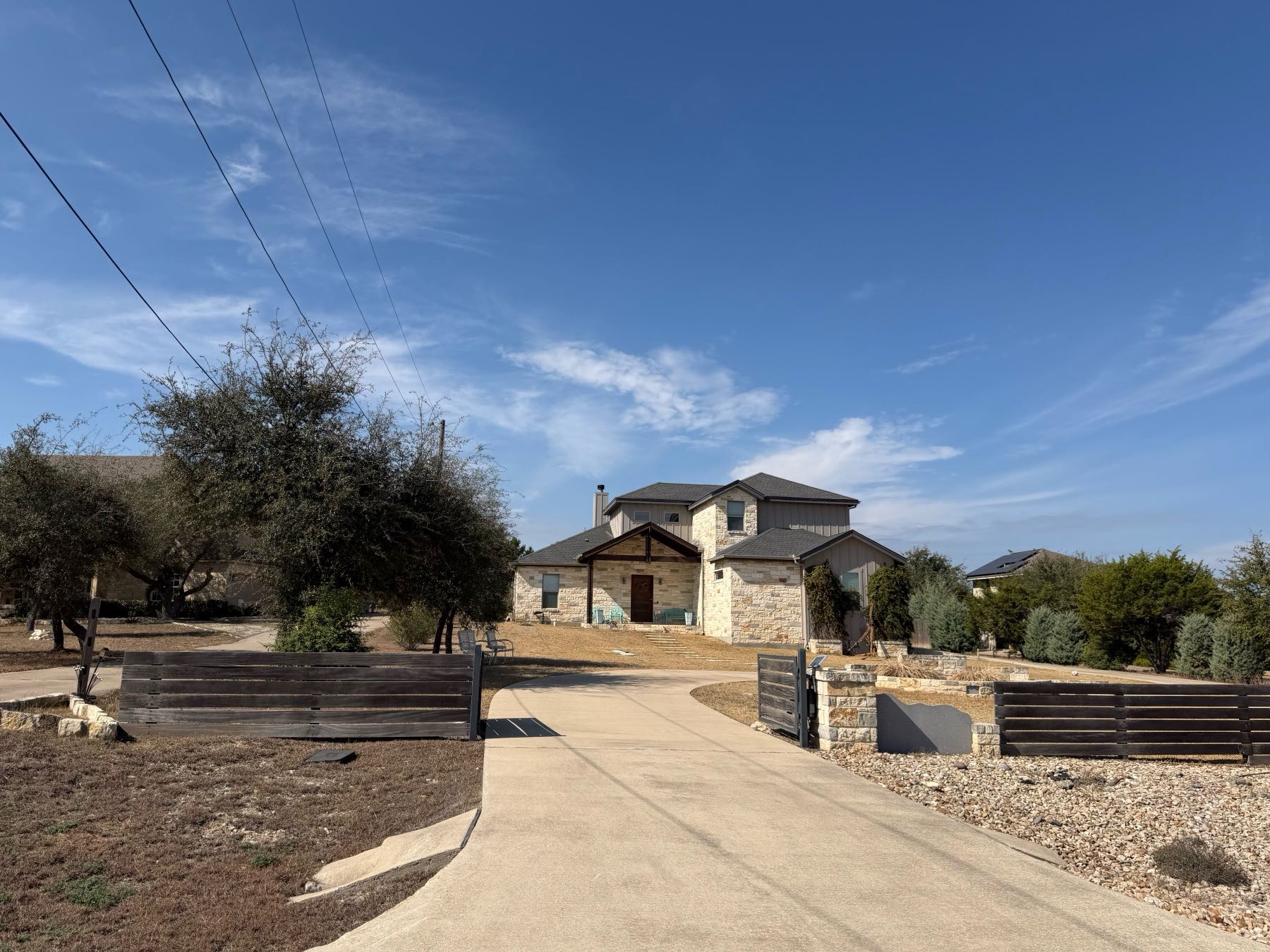 Stone home with modern horizontal wood and metal driveway security gate in Sunset Canyon, Dripping Springs TX 78620