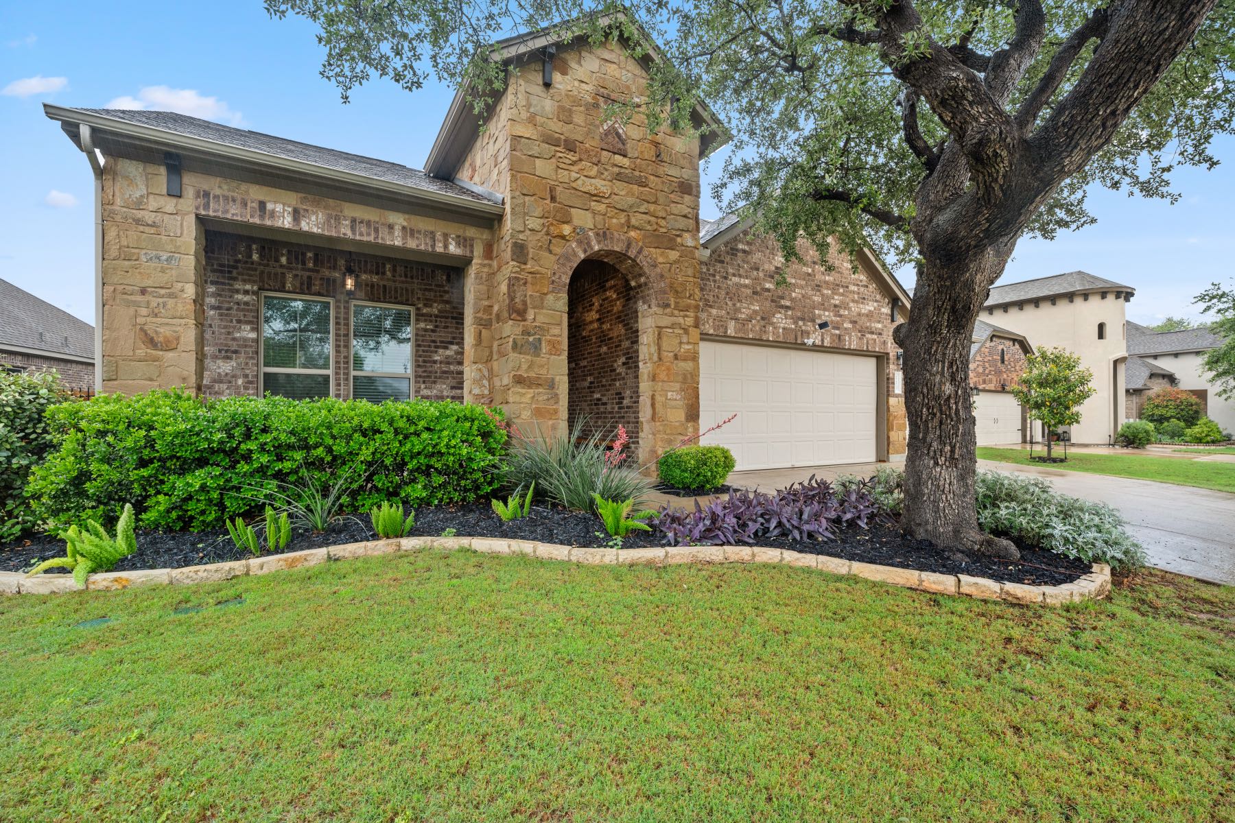 Stone and brick facade with arched front entry and landscaping on an Austin area home