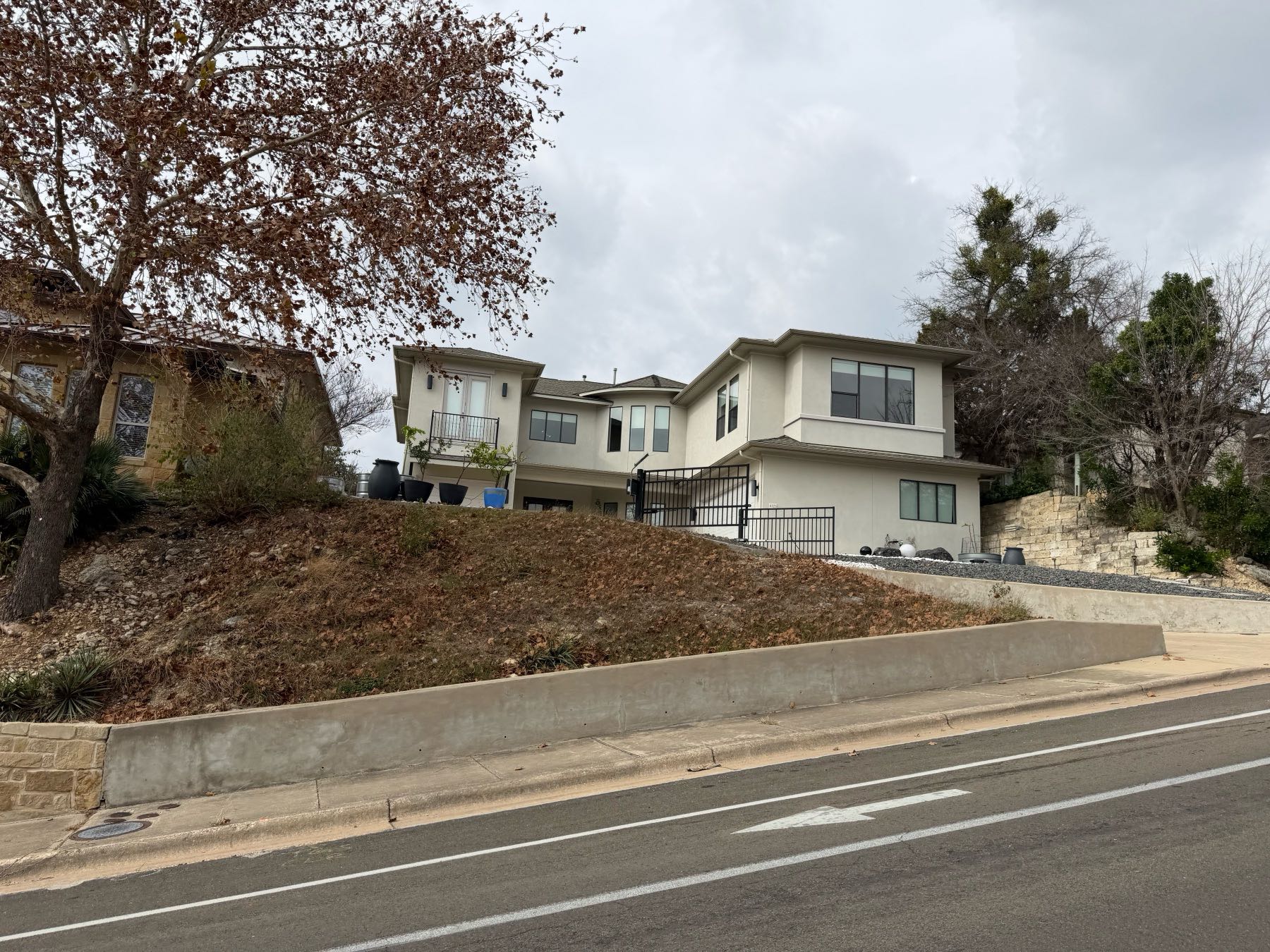 Modern updated two story stucco home elevated above street with retaining wall in Great Hills Austin TX