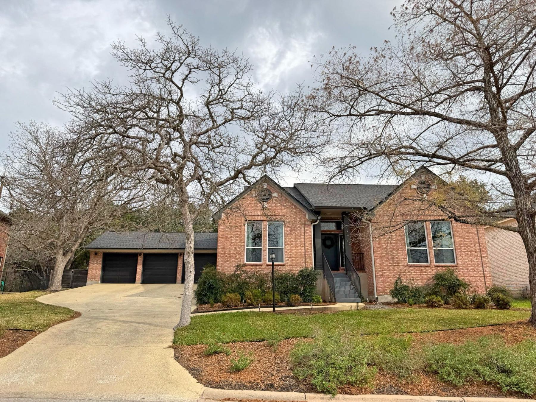 One story red brick home with dark two car garage and mature trees in Great Hills Austin TX
