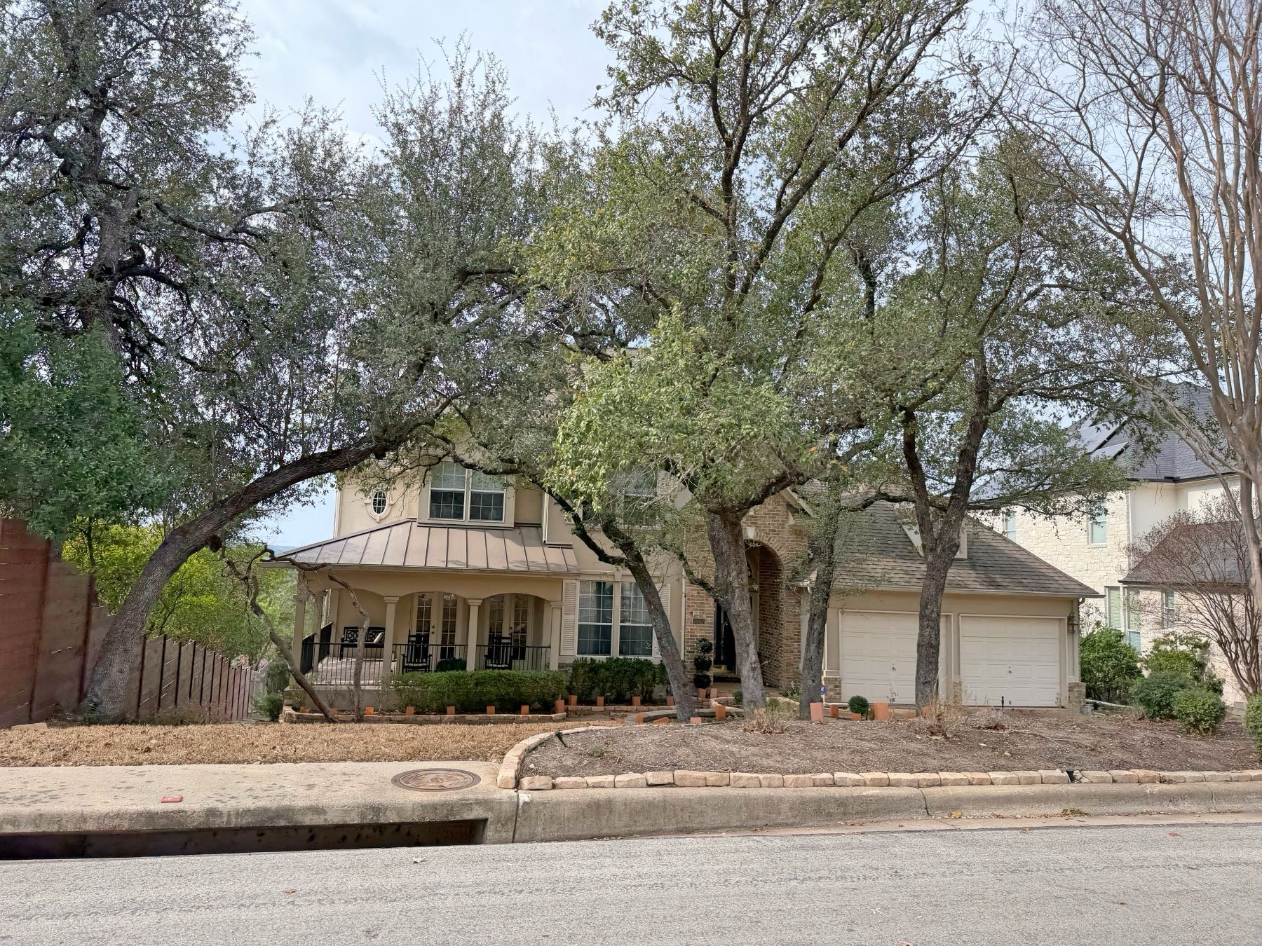 Two story home with metal roof accent covered porch and mature trees in Great Hills Austin TX