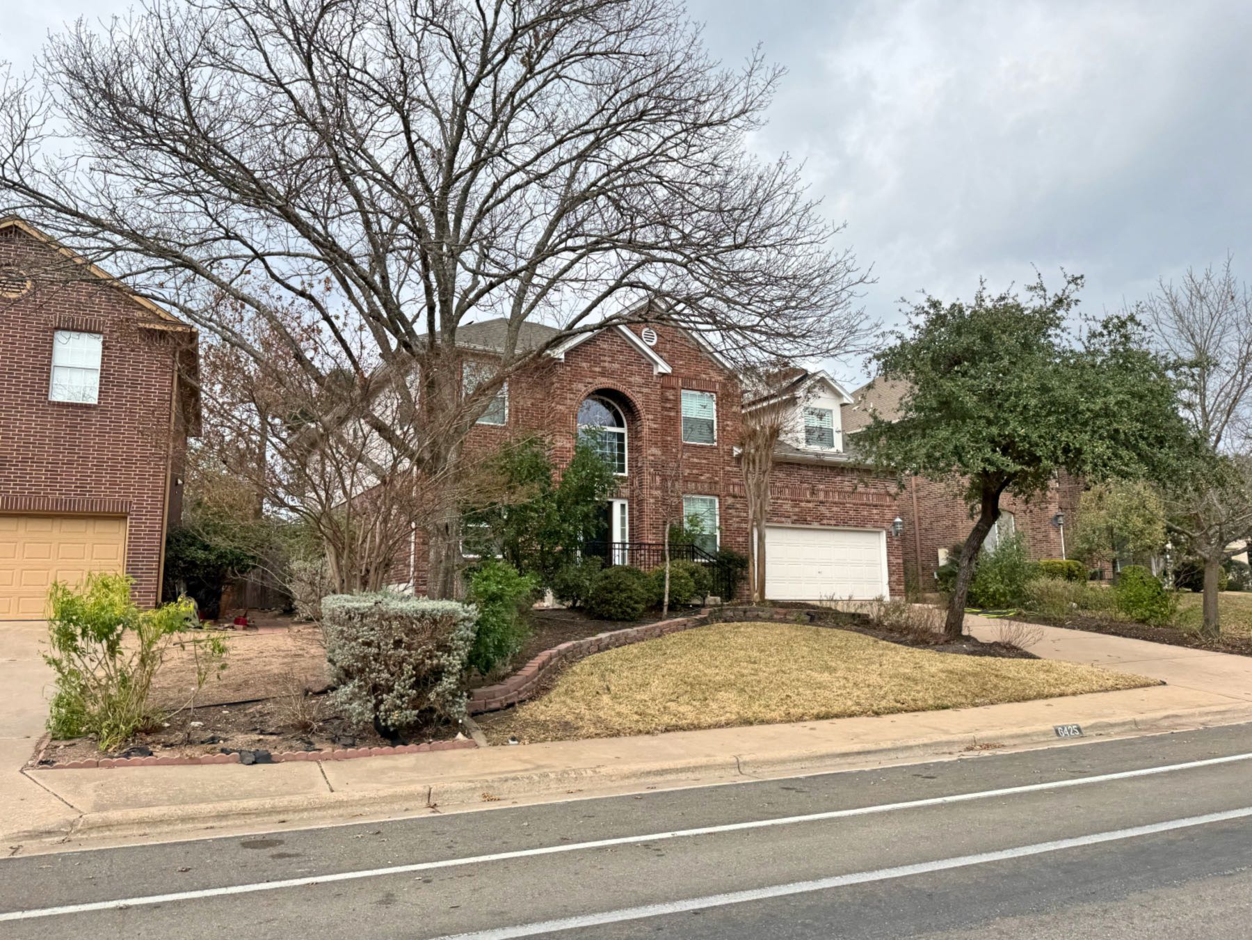 Two story red brick home on main road with large oak tree in Great Hills Austin TX 78759