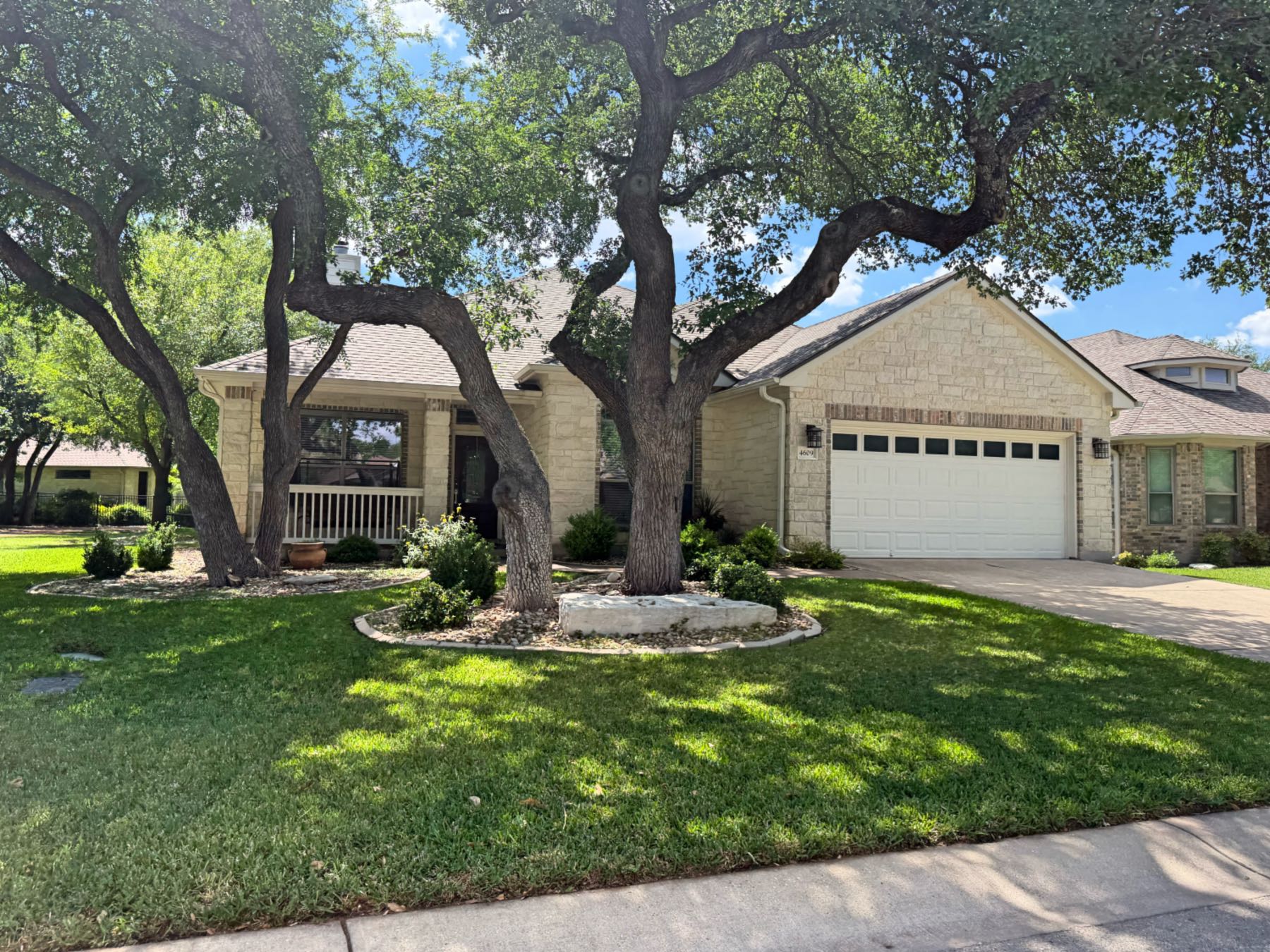 Limestone home with mature oak trees and covered front porch in Heritage Oaks Georgetown TX 78633