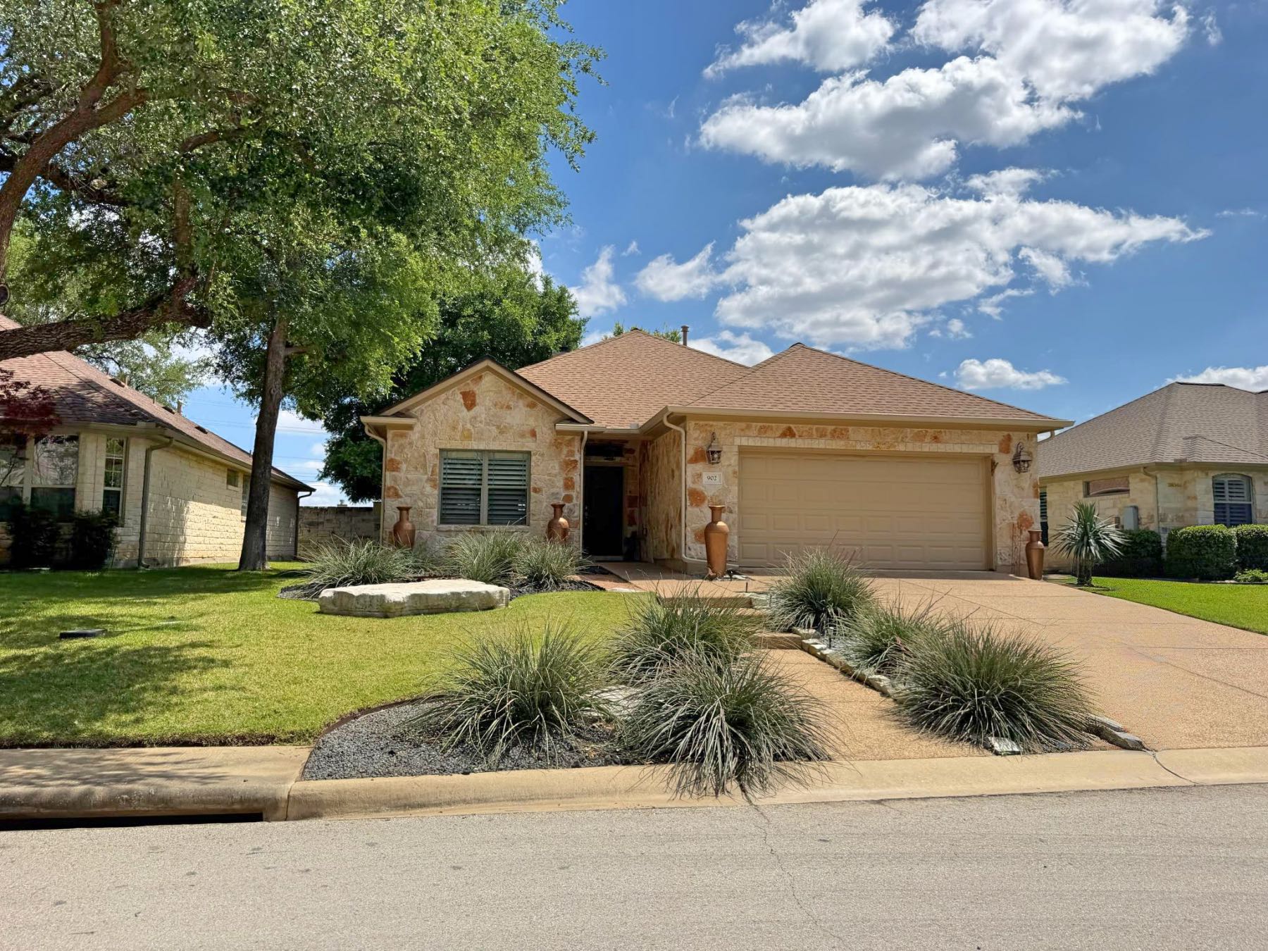 Stone home with ornamental grass landscaping and decorative urns at entry in Heritage Oaks Georgetown TX 78633