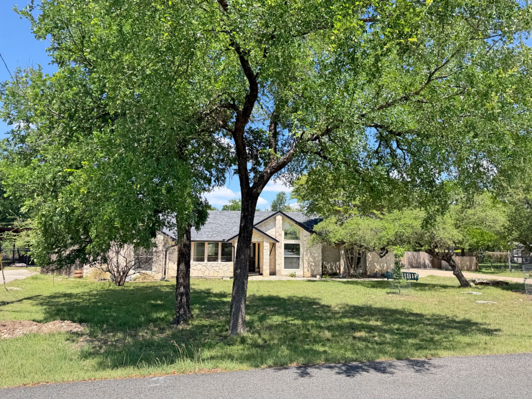 Stone home partially hidden beneath a large mature oak tree canopy on an open green yard in Serenada, Georgetown TX 78628