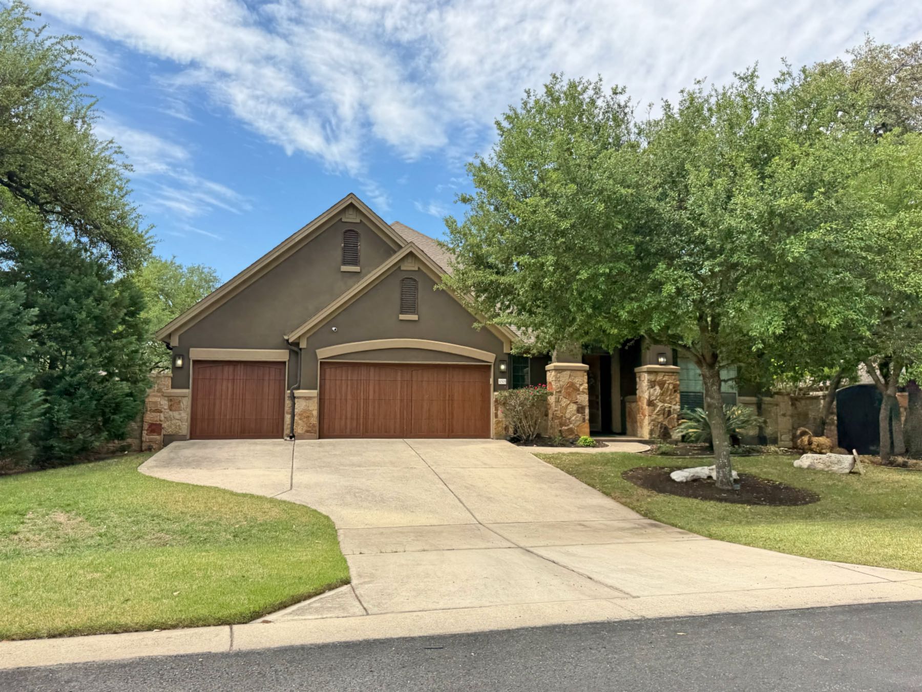 Dark olive stucco home in Brodie Springs Austin 78748 with three-car garage featuring natural wood doors and stone accent columns