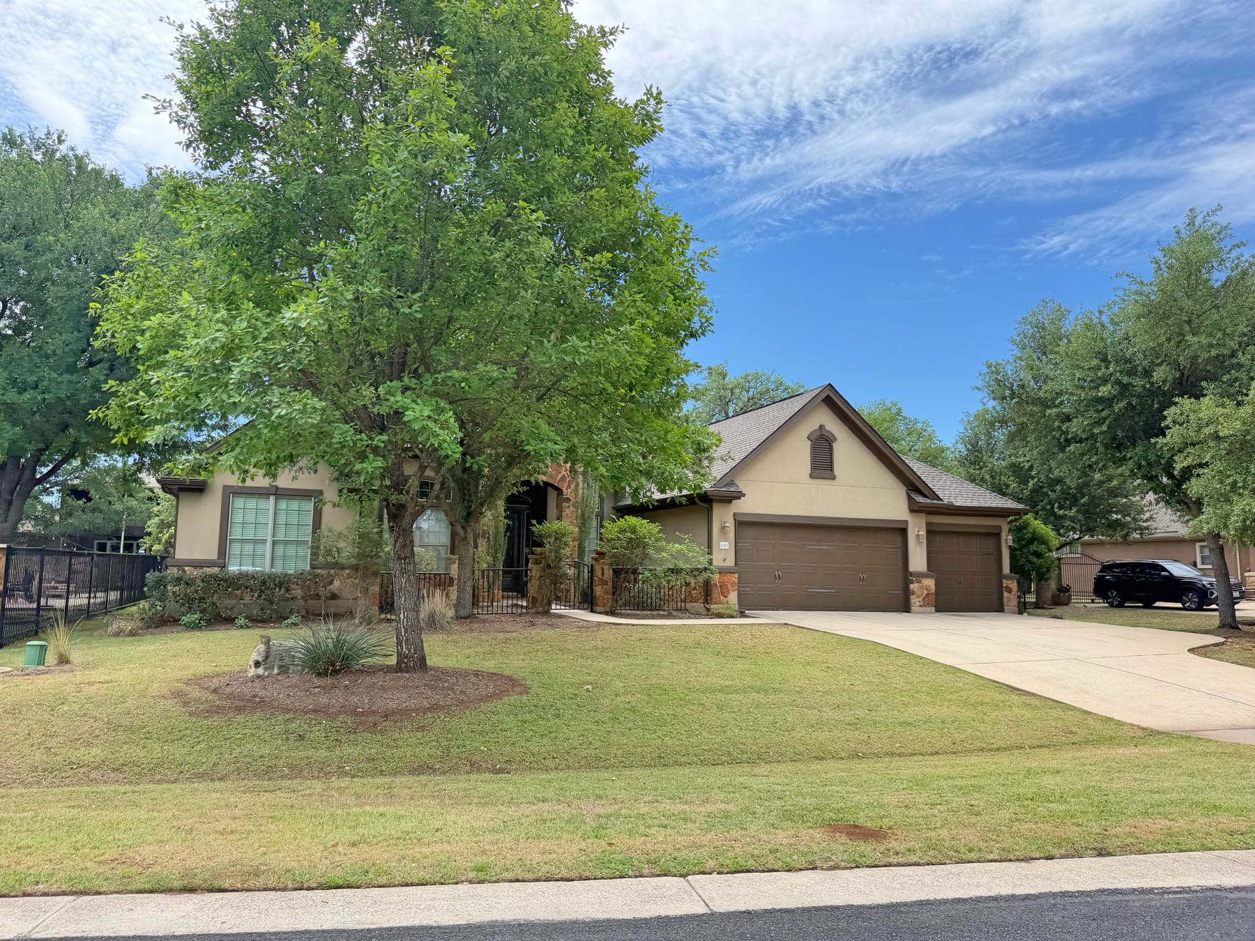 Single-story stucco and stone home in Brodie Springs Austin 78748 with wide two-car garage and mature shade trees flanking the property