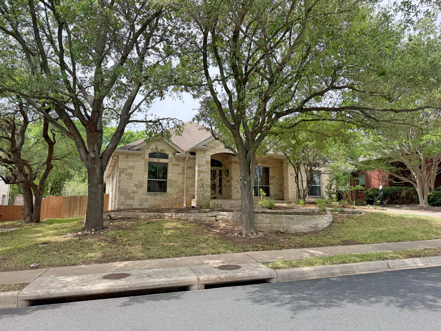 Single story limestone home with stone retaining wall and mature oak trees in Estates of Bauerle Ranch Austin TX 78748