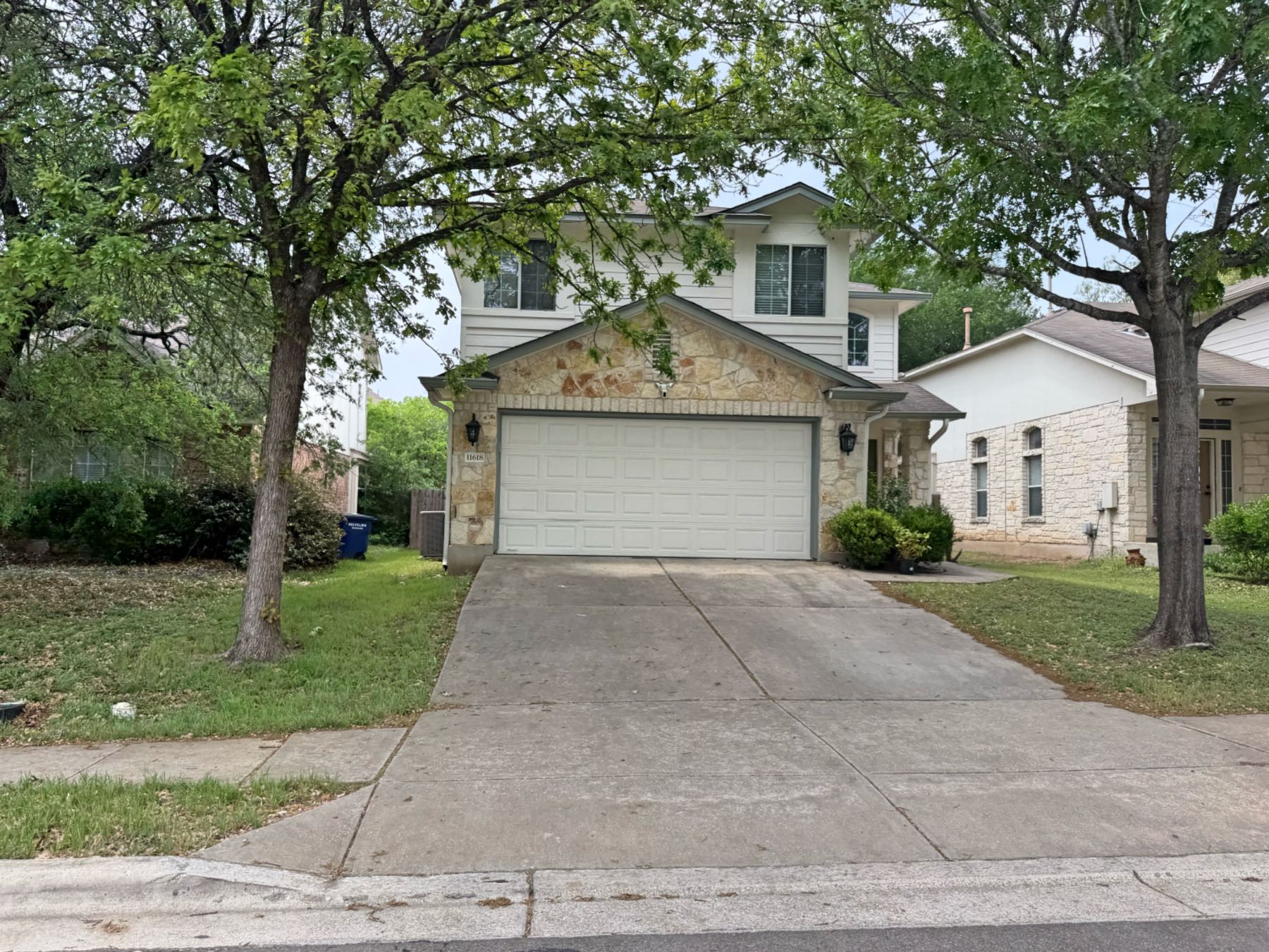 Two story stone and siding home with two car garage and mature oak trees in Olympic Heights Austin TX 78748