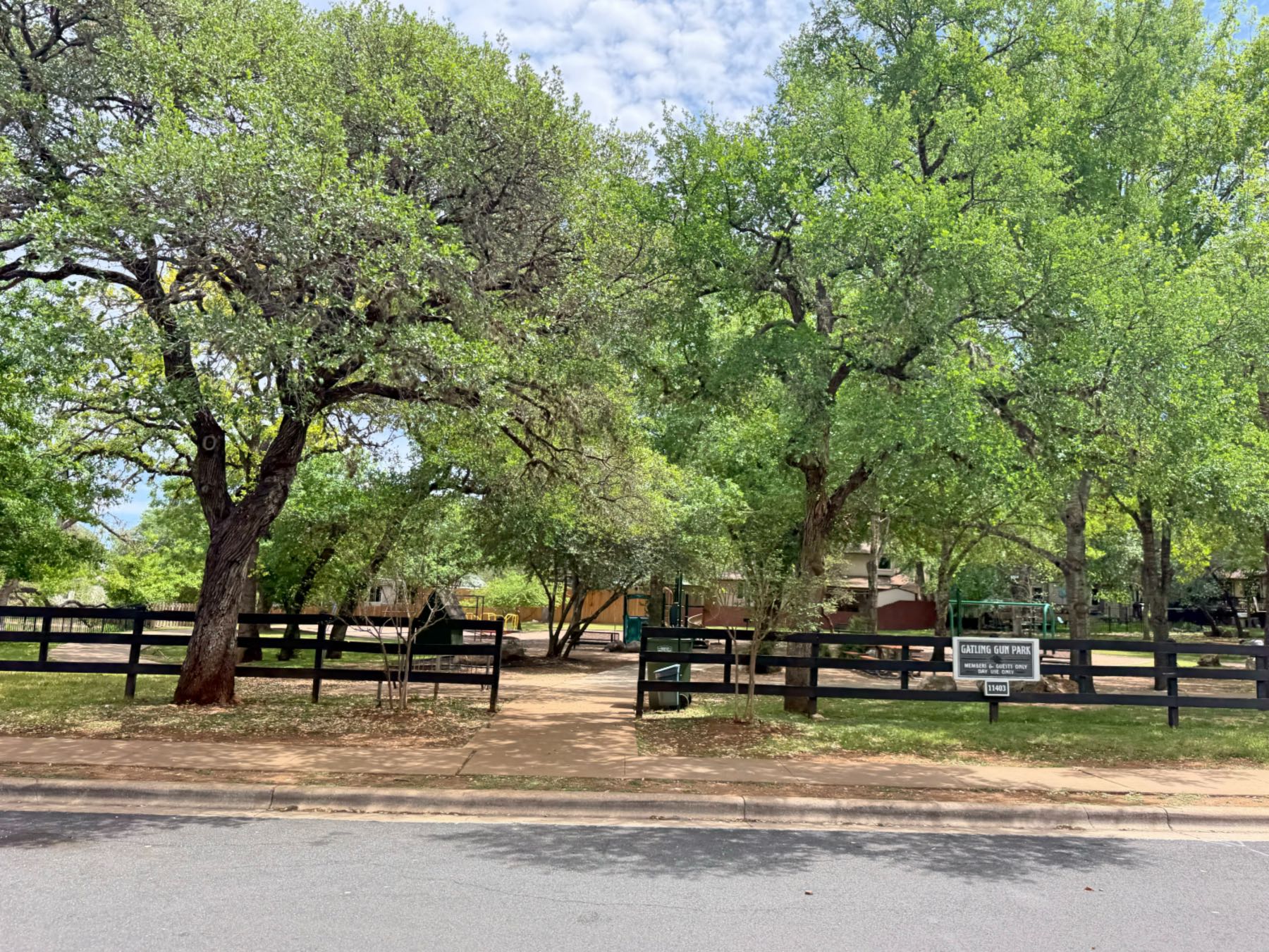 Shady Hollow community park with black split rail fence and canopy of mature oak trees in Austin TX 78748