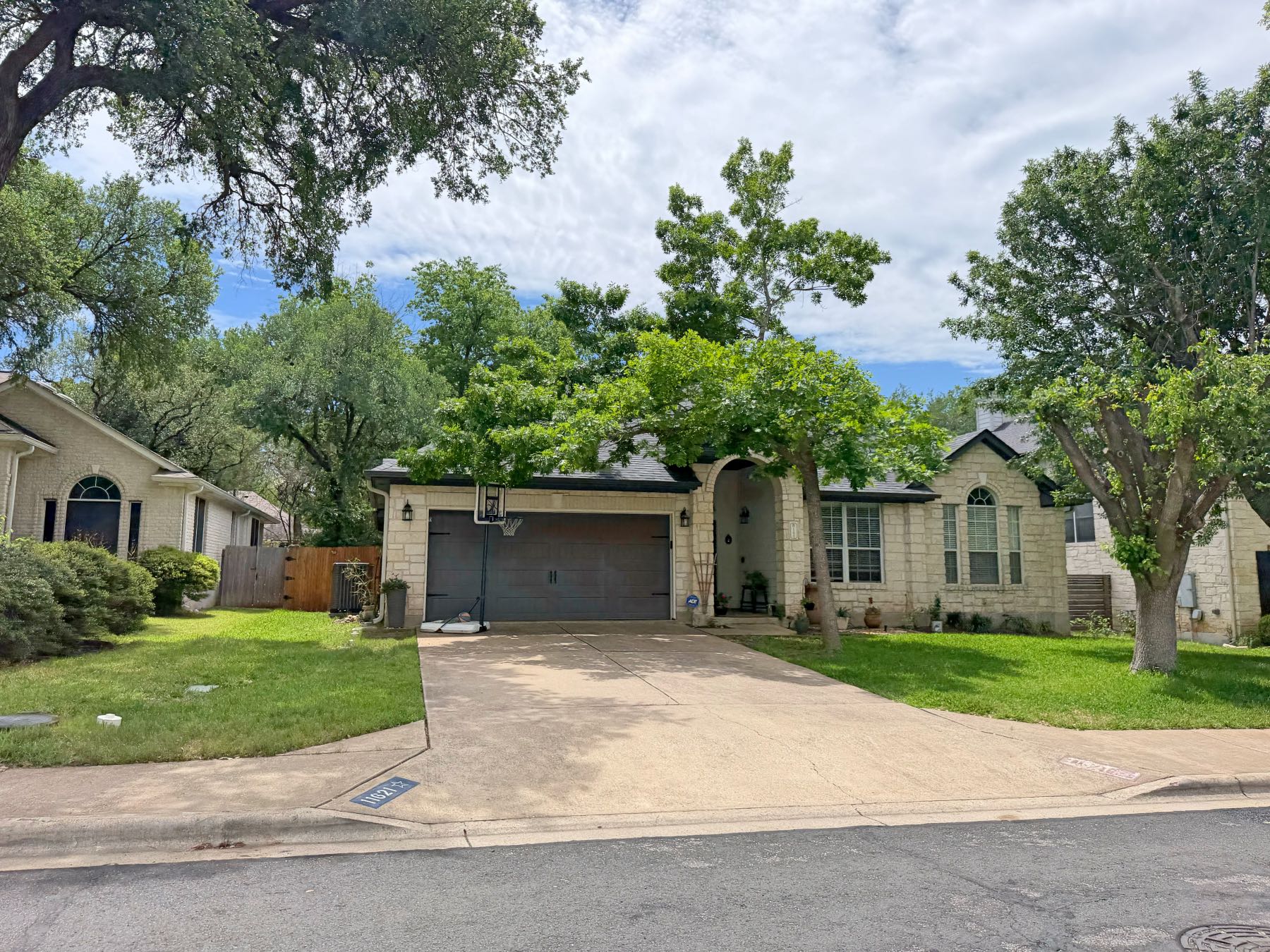 Stone home with dark garage door and arched entryway surrounded by mature trees in Southland Oaks Austin TX 78748
