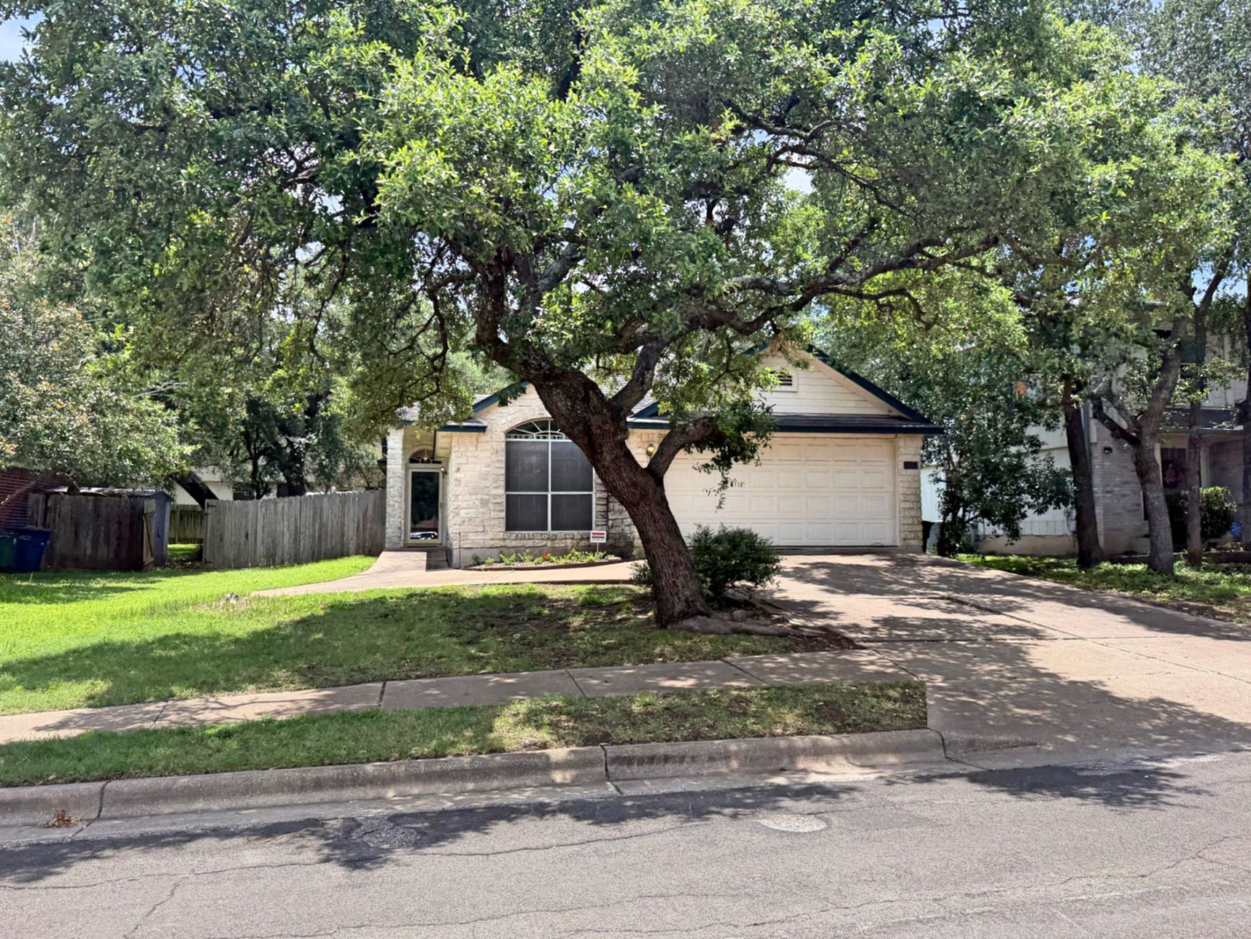 Single-story stone home in Parkwood Austin TX 78748 shaded by a large live oak tree